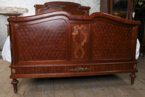 fig 2. An antique French mahogany bed frame featuring geometric parquetry panels, fruitwood ribbon marquetry on the footboard, and gilt bronze mounts.