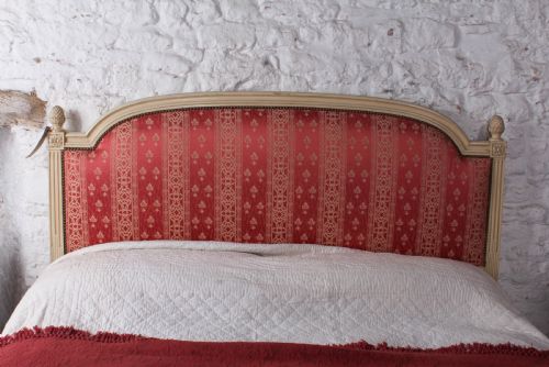 fig 3. A French Louis XVI style king size bedstead featuring a cream painted carved timber frame and red patterned damask upholstered headboard and footboard.
