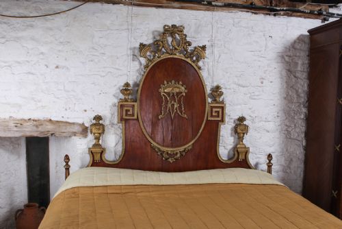 fig 1. An antique mahogany super king bed featuring a high headboard with an oval central medallion, carved giltwood crest, Greek key motifs, and turned posts.