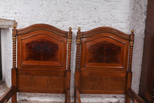 fig 1. A pair of matching continental mahogany single beds featuring arched headboards, flame veneer panels, spiral turned posts, and gilt pineapple finials.