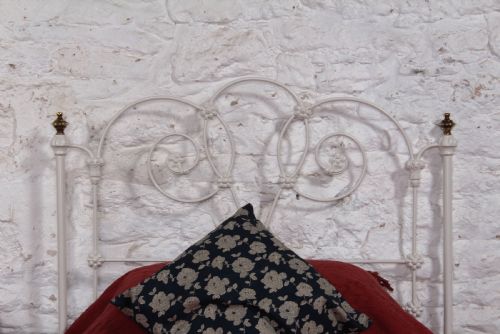 fig 4. A Victorian white painted wrought iron single bed frame featuring ornate scrollwork, floral metal castings, turned brass finials, and castors.
