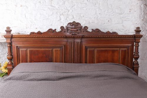 fig 1. A carved solid walnut emperor size bedstead featuring a cresting motif, geometric panelled headboard and footboard, and turned posts.
