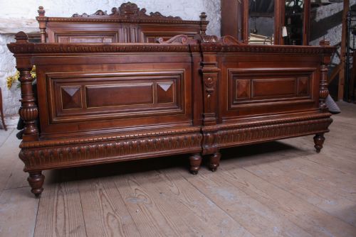 fig 2. A carved solid walnut emperor size bedstead featuring a cresting motif, geometric panelled headboard and footboard, and turned posts.
