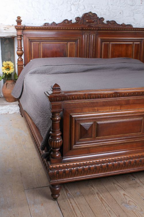 fig 3. A carved solid walnut emperor size bedstead featuring a cresting motif, geometric panelled headboard and footboard, and turned posts.
