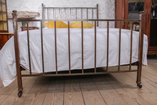 fig 1. An antique Victorian king-size bed frame featuring vertical brass spindles, square corner posts, and an aged metallic patina set on castors.