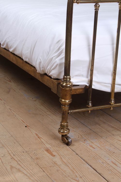 fig 1. An antique French brass single bed frame featuring an arched headboard and footboard decorated with circular hoop motifs and vertical spindles.