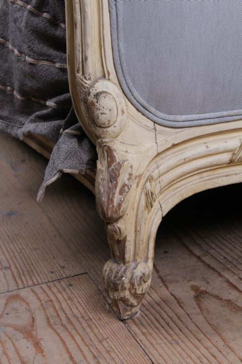fig 2. An antique French king-size bed featuring a cream painted carved wooden frame and light grey upholstered panels on the headboard and footboard.