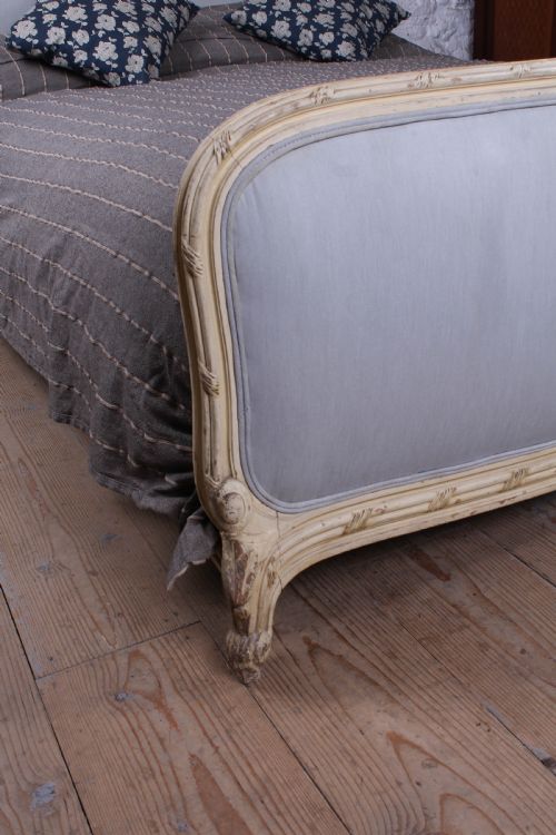 fig 4. An antique French king-size bed featuring a cream painted carved wooden frame and light grey upholstered panels on the headboard and footboard.