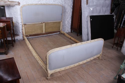 fig 5. An antique French king-size bed featuring a cream painted carved wooden frame and light grey upholstered panels on the headboard and footboard.