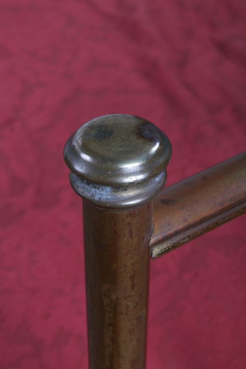 fig 2. An antique single brass bedstead featuring vertical tubular spindles and a matching headboard and footboard with brass finials.