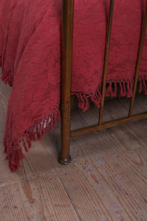fig 3. An antique single brass bedstead featuring vertical tubular spindles and a matching headboard and footboard with brass finials.