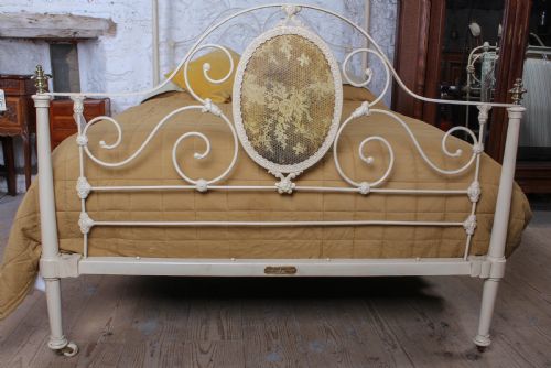 fig 1. A cream painted wrought iron king size half tester bed frame featuring an ornate scrollwork footboard with a central oval medallion and brass finials.