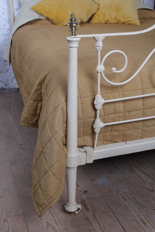 fig 4. A cream painted wrought iron king size half tester bed frame featuring an ornate scrollwork footboard with a central oval medallion and brass finials.