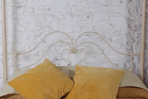 fig 5. A cream painted wrought iron king size half tester bed frame featuring an ornate scrollwork footboard with a central oval medallion and brass finials.
