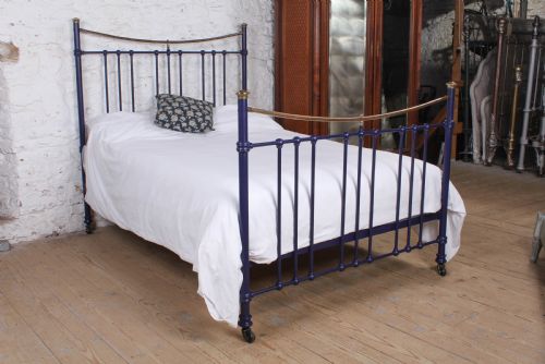 fig 1. A Victorian metal double bedstead featuring a dark blue painted frame, vertical spindles, dipped brass top rails, and brass corner finials.