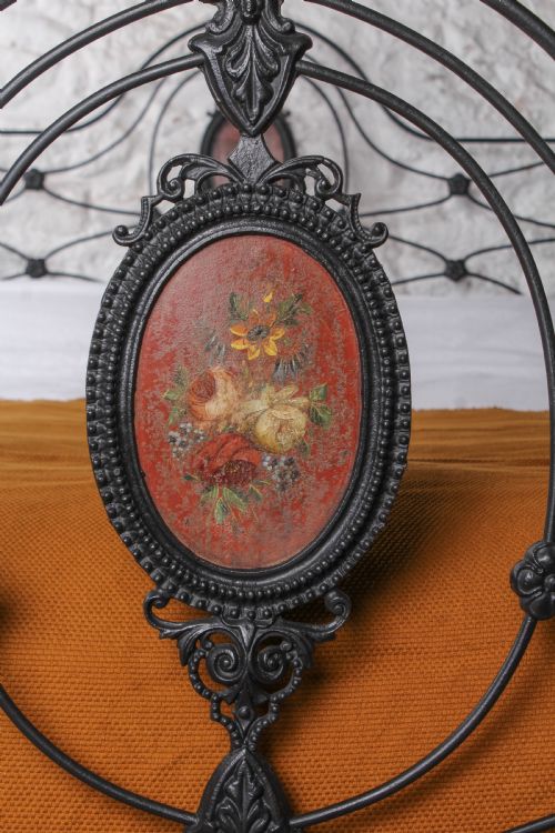 fig 2. A Victorian black-painted cast iron bedstead featuring brass finials, arched lattice scrollwork, and oval floral enamel medallions on the headboard and footboard.