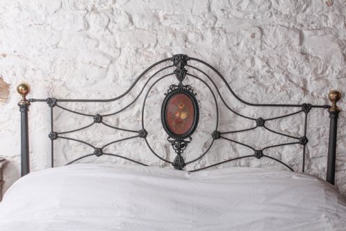 fig 4. A Victorian black-painted cast iron bedstead featuring brass finials, arched lattice scrollwork, and oval floral enamel medallions on the headboard and footboard.