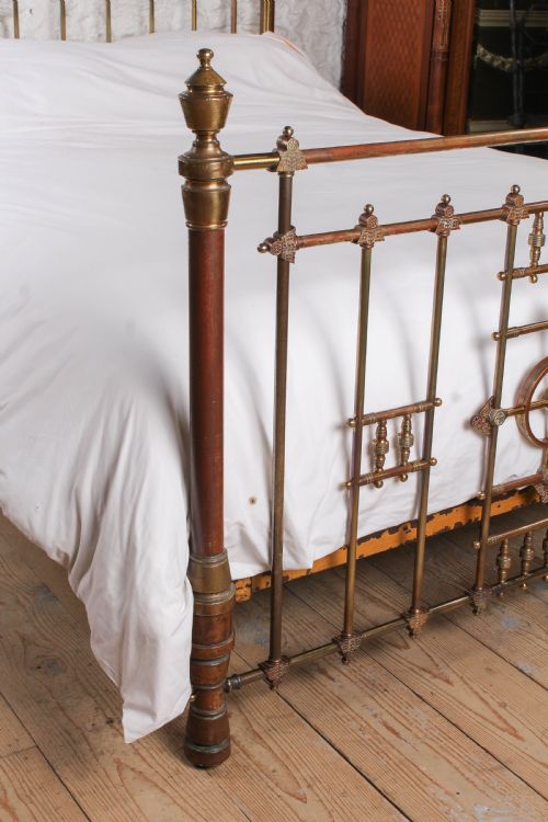 fig 3. A Victorian king-size brass bed frame featuring detailed vertical spindles, geometric central motifs on the footboard, and turned corner posts with finials.