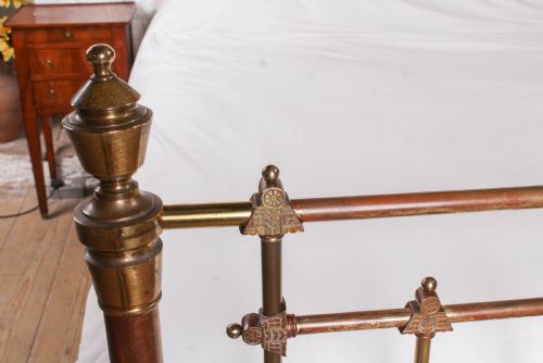fig 4. A Victorian king-size brass bed frame featuring detailed vertical spindles, geometric central motifs on the footboard, and turned corner posts with finials.