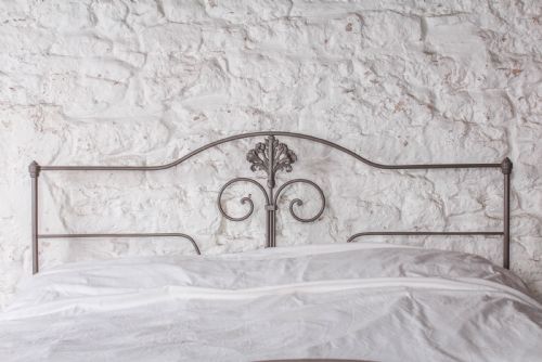 fig 3. A king size Portuguese iron bed frame painted in a neutral taupe colour, featuring decorative scrollwork and a central shell motif on both the headboard and footboard.