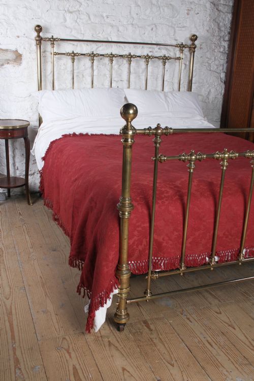 fig 1. An antique king-sized brass bedstead featuring turned vertical spindles, corner post finials, and a warm aged patina.