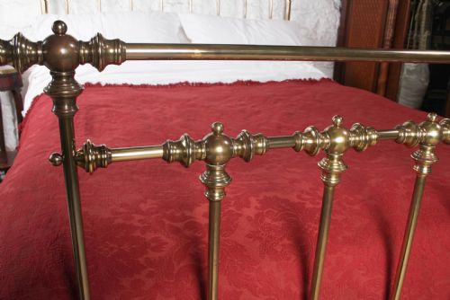 fig 4. An antique king-sized brass bedstead featuring turned vertical spindles, corner post finials, and a warm aged patina.