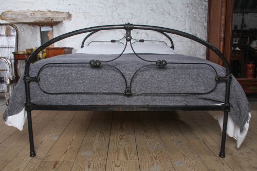 fig 1. An antique dark wrought iron double bed frame featuring arched headboard and footboard rails with decorative cast rosettes.