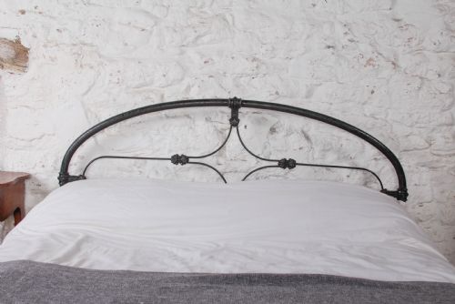 fig 4. An antique dark wrought iron double bed frame featuring arched headboard and footboard rails with decorative cast rosettes.
