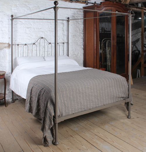 fig 1. A low height king size metal four poster bed frame with slender corner posts, brass finials, and an arched headboard with vertical iron spindles.