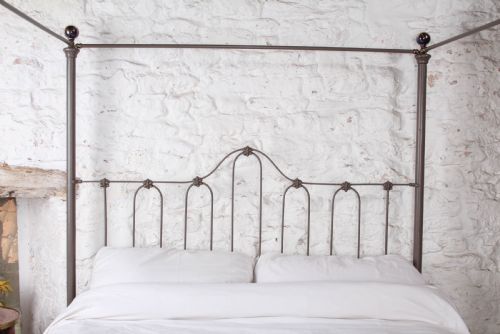 fig 3. A low height king size metal four poster bed frame with slender corner posts, brass finials, and an arched headboard with vertical iron spindles.