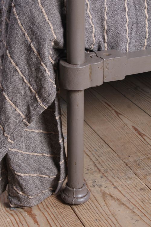 fig 4. A low height king size metal four poster bed frame with slender corner posts, brass finials, and an arched headboard with vertical iron spindles.