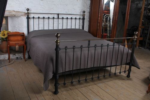 fig 1. A super king size bedstead featuring a black iron frame with vertical spindles, cast rosettes, and brass top rails with brass ball finials.