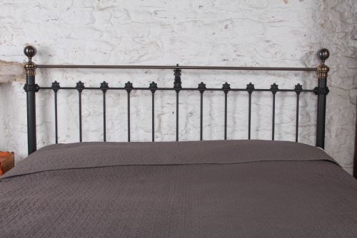 fig 4. A super king size bedstead featuring a black iron frame with vertical spindles, cast rosettes, and brass top rails with brass ball finials.