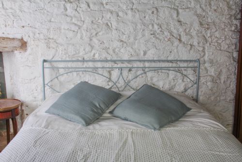 fig 1. A light blue painted forged iron king-size bedstead featuring a simple arched headboard with decorative scrollwork.