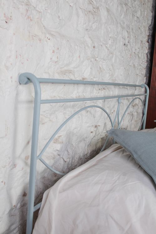 fig 3. A light blue painted forged iron king-size bedstead featuring a simple arched headboard with decorative scrollwork.