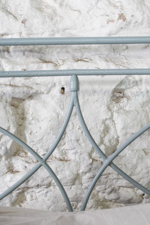 fig 4. A light blue painted forged iron king-size bedstead featuring a simple arched headboard with decorative scrollwork.
