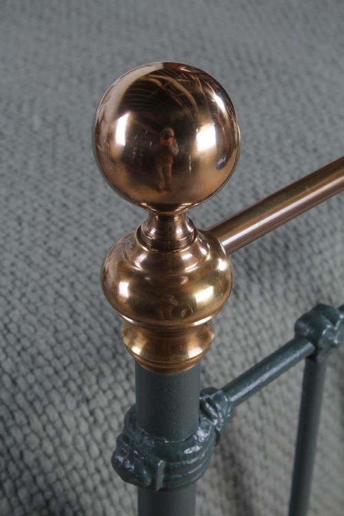 fig 1. A Victorian metal bedstead featuring dark green painted iron uprights, vertical spindles, brass top rails, and brass finials.