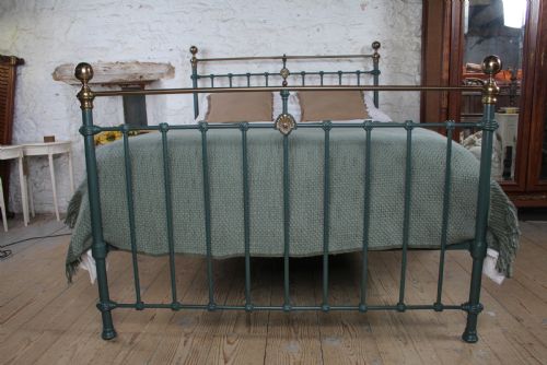 fig 3. A Victorian metal bedstead featuring dark green painted iron uprights, vertical spindles, brass top rails, and brass finials.