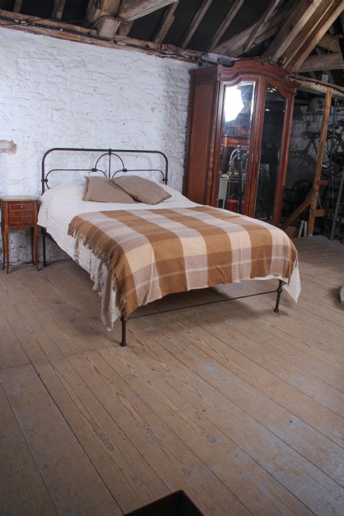 fig 1. An antique dark iron king size bedstead featuring an arched headboard with decorative scrollwork and a low footrail design.