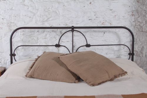 fig 2. An antique dark iron king size bedstead featuring an arched headboard with decorative scrollwork and a low footrail design.