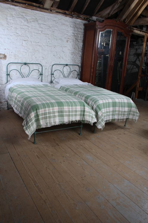fig 1. A pair of green painted iron single bed frames featuring scrolled Celtic heart motifs on the headboards and low open ends.