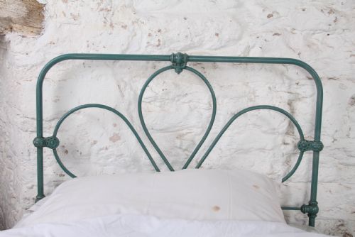 fig 2. A pair of green painted iron single bed frames featuring scrolled Celtic heart motifs on the headboards and low open ends.