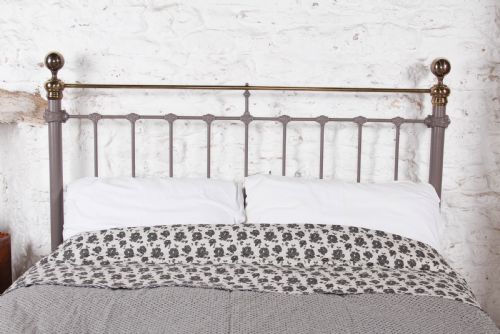 fig 3. A Victorian cast iron and brass king size bedstead featuring vertical spindles, decorative brass finials, and a grey painted frame.