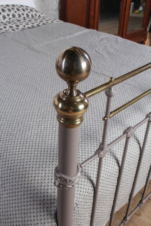 fig 4. A Victorian cast iron and brass king size bedstead featuring vertical spindles, decorative brass finials, and a grey painted frame.