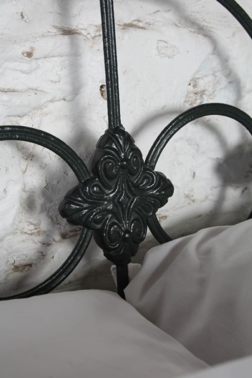 fig 2. An antique king-size black cast iron bed frame featuring a curved tubular headboard with central cast details and no footboard.