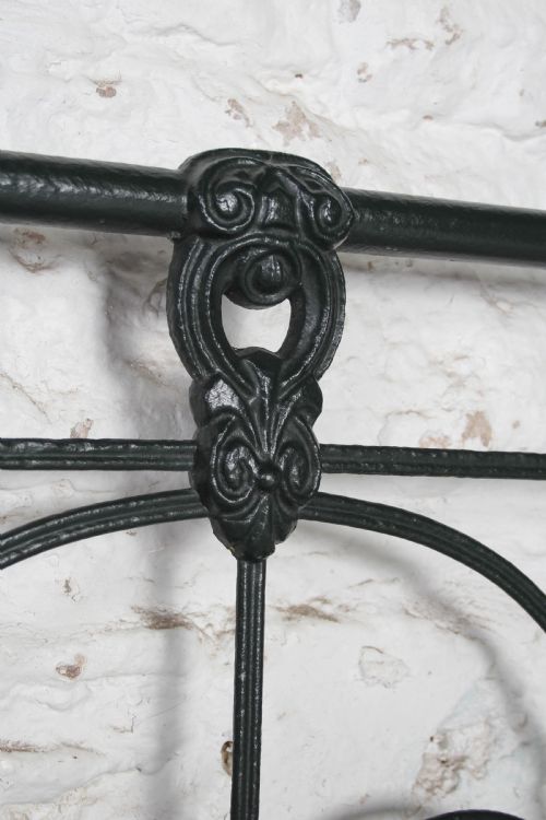 fig 3. An antique king-size black cast iron bed frame featuring a curved tubular headboard with central cast details and no footboard.