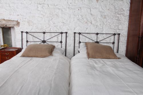 fig 3. A pair of dark Victorian wrought iron single beds with geometric headboards and footless frames.