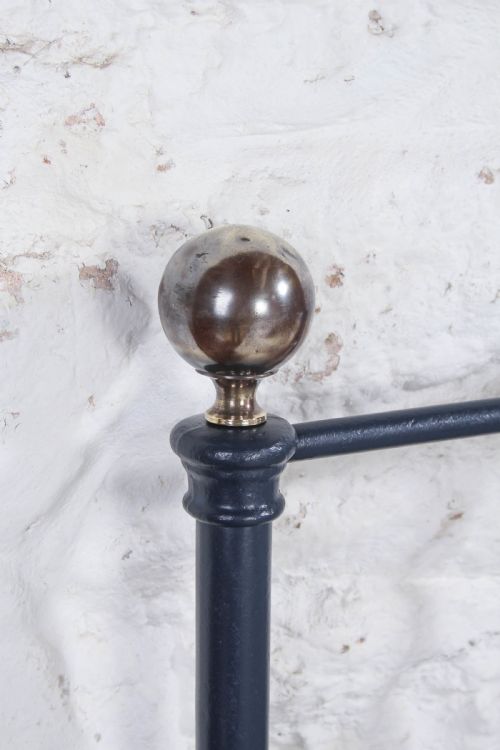 fig 3. A Victorian style king size dark blue cast iron bedstead featuring decorative brass finials and a low footboard.