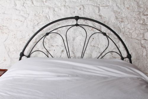 fig 1. A Victorian black wrought iron king-size bed frame featuring an arched headboard with decorative scrollwork loops and a low footboard.