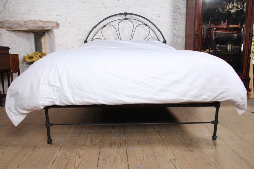 fig 4. A Victorian black wrought iron king-size bed frame featuring an arched headboard with decorative scrollwork loops and a low footboard.